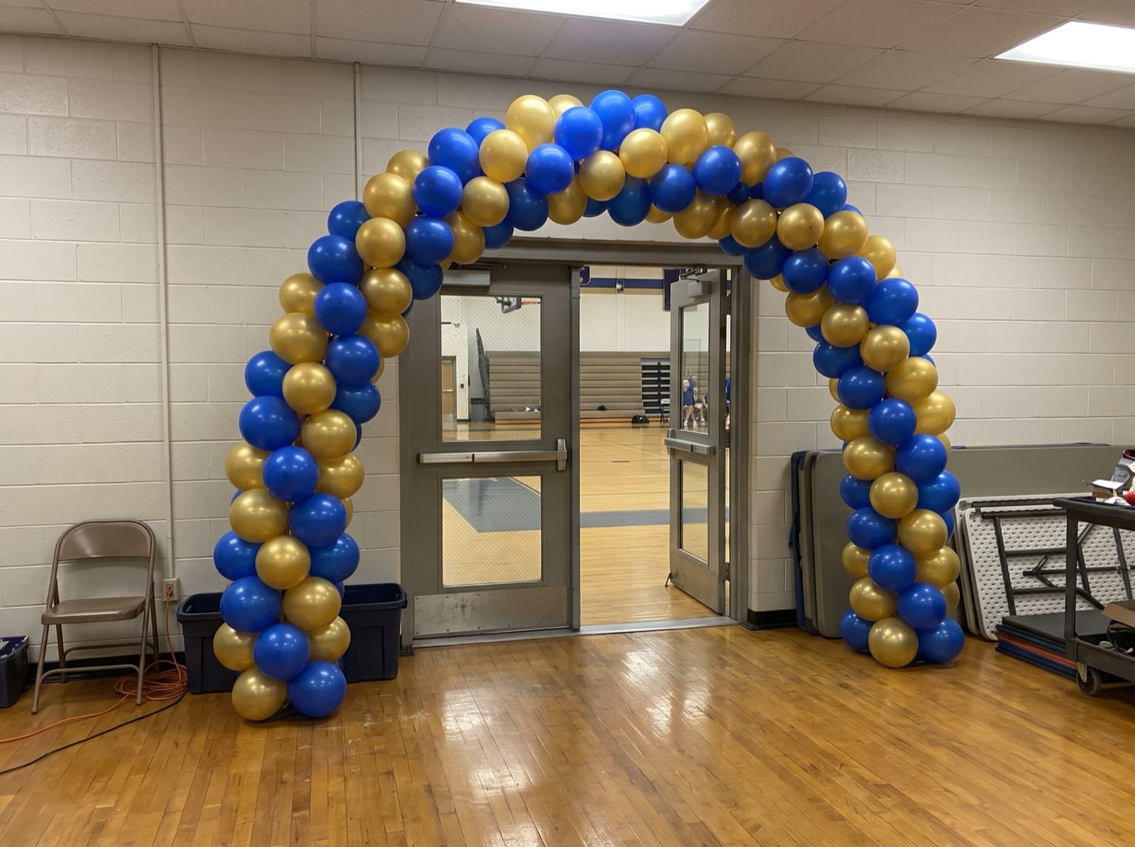 Spiral balloon arch in blue and gold over a school gym entrance