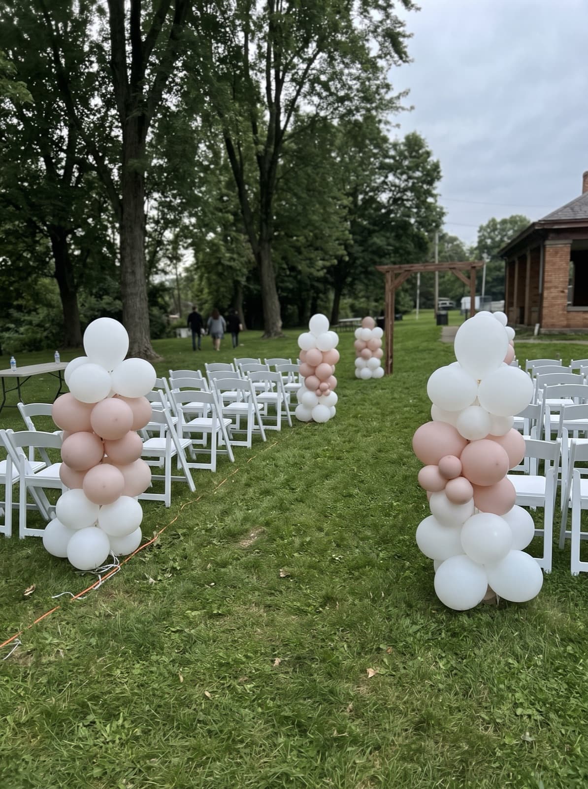 Organic balloon columns lining an outdoor ceremony aisle