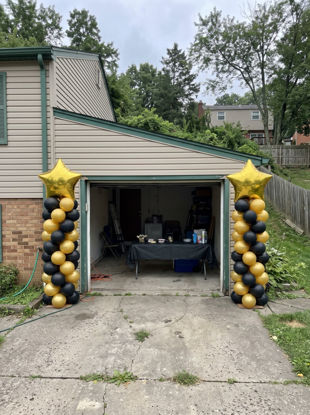 Pair of spiral balloon columns in black and gold with star toppers beside a garage at a graduation party