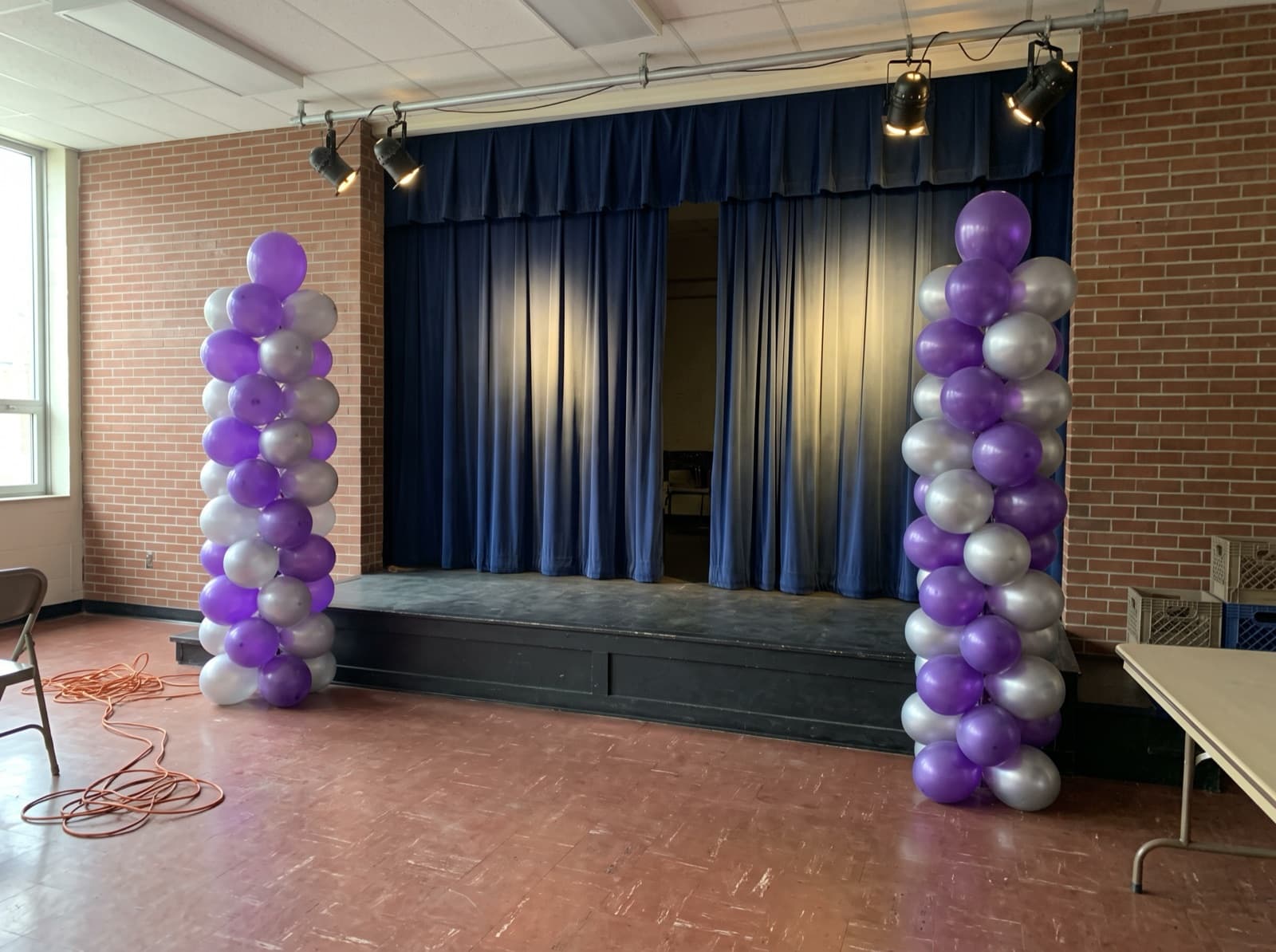 Purple and silver balloon columns bookending a school stage