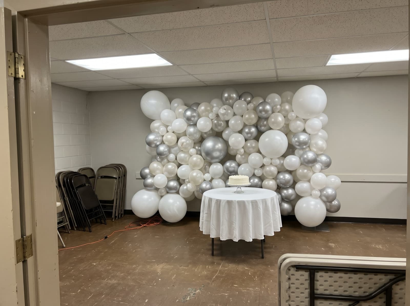 Organic balloon wall in white, pearl and silver behind a cake table in a Pittsburgh church social hall